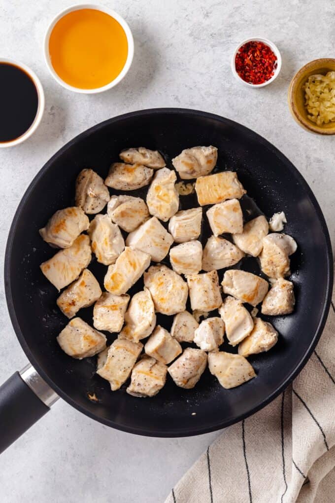 Cubed chicken breast pieces being cooked in a skillet.