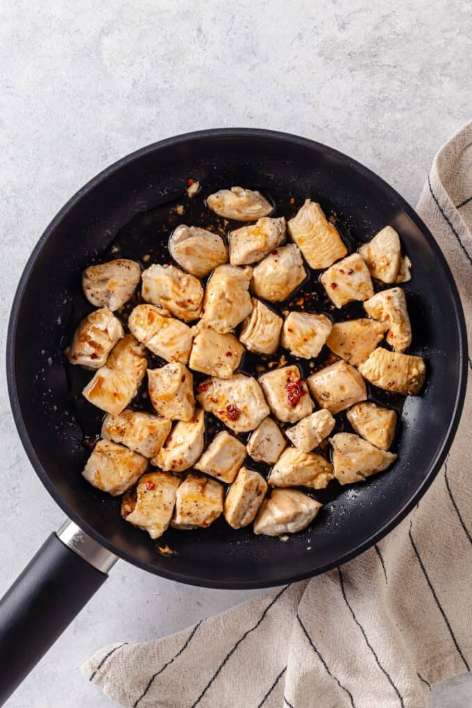 A soy sauce mixture added to cubed chicken breasts cooking in a large skillet.
