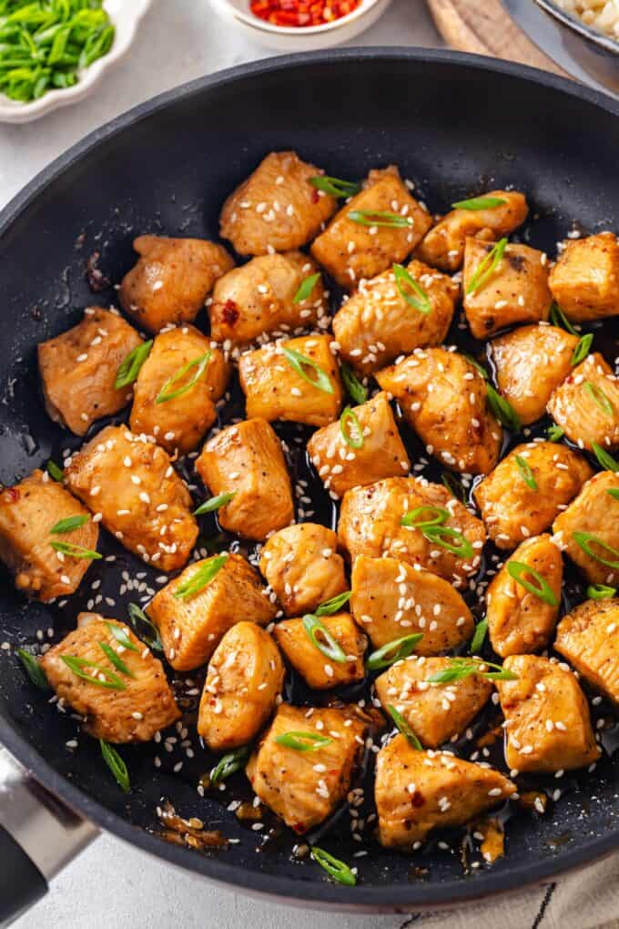 A saucy honey garlic chicken skillet with sesame seeds and sliced green onions sprinkled on top.