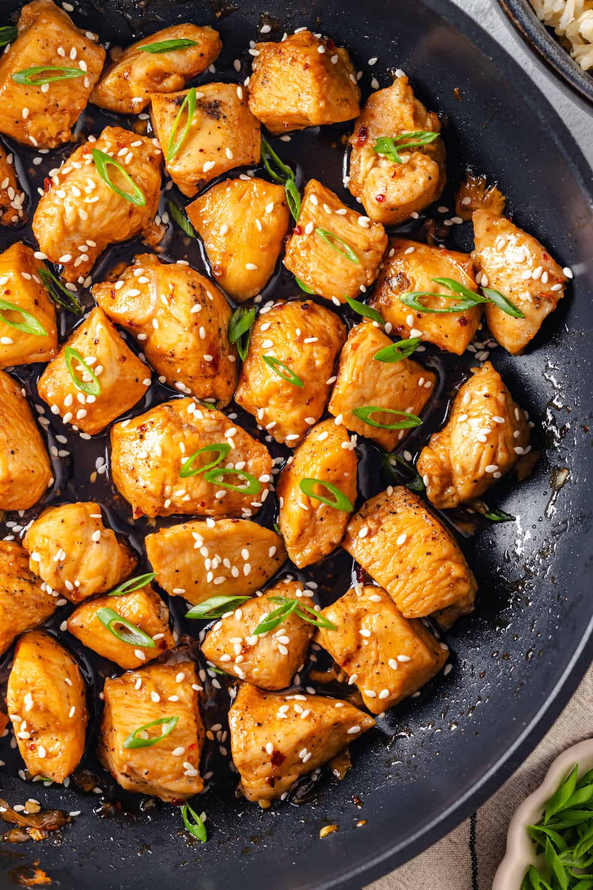 Close up of a saucy honey garlic chicken skillet with sesame seeds and sliced green onions sprinkled on top.
