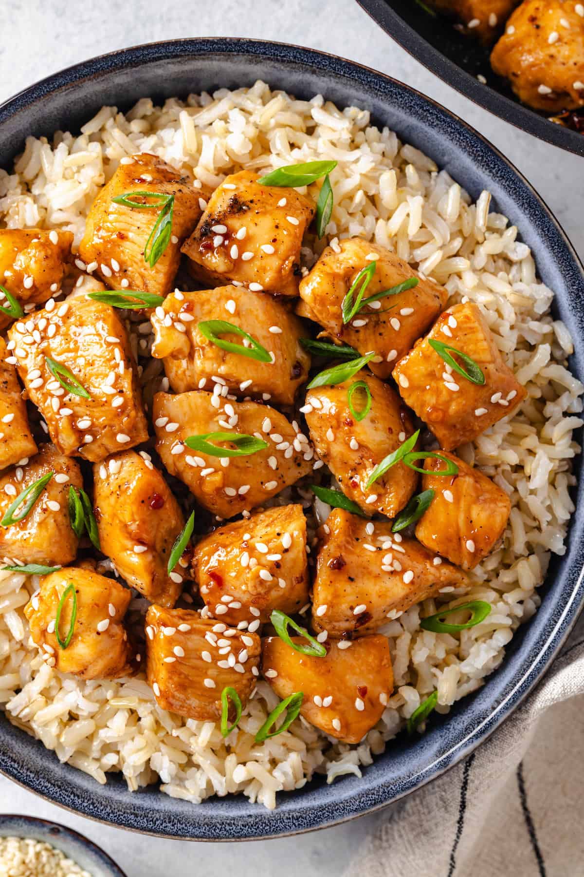 Honey garlic chicken pieces served over steamed rice with sesame seeds and sliced green onions sprinkled on top.