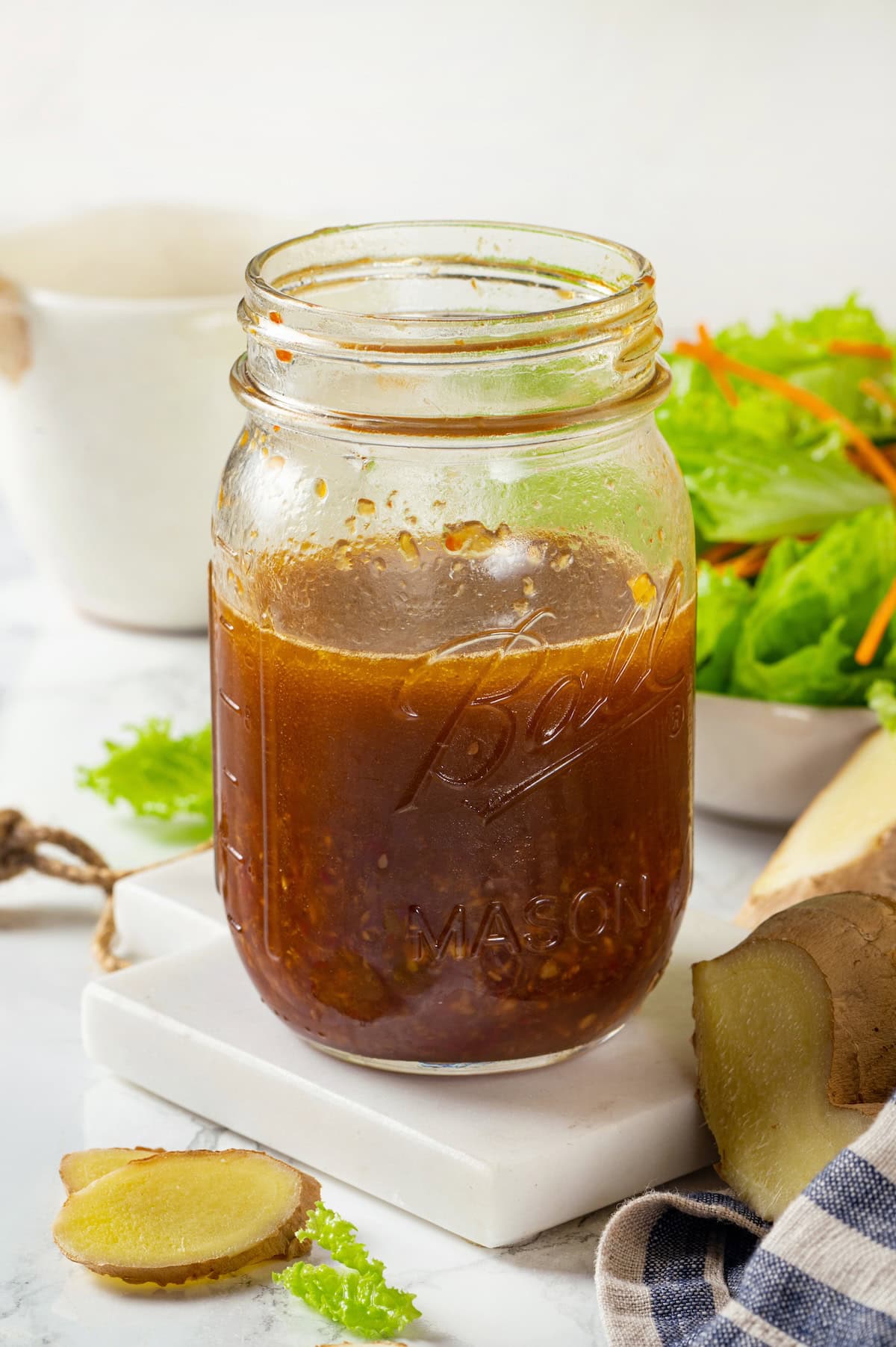 A glass jar with a homemade soy ginger vinaigrette with sliced ginger pieces to the side.