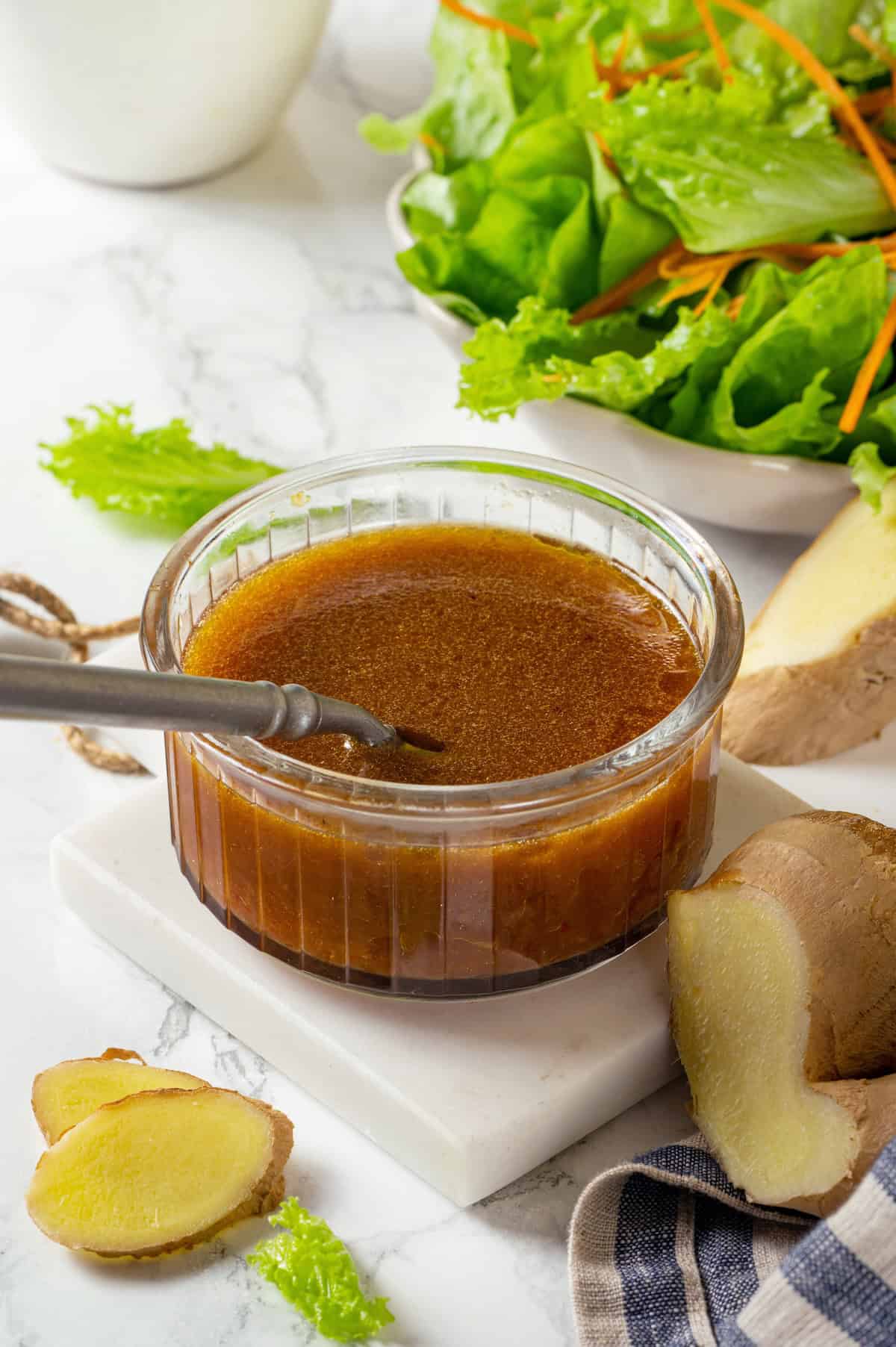 A glass container full of a homemade soy ginger dressing with a spoon resting in it.