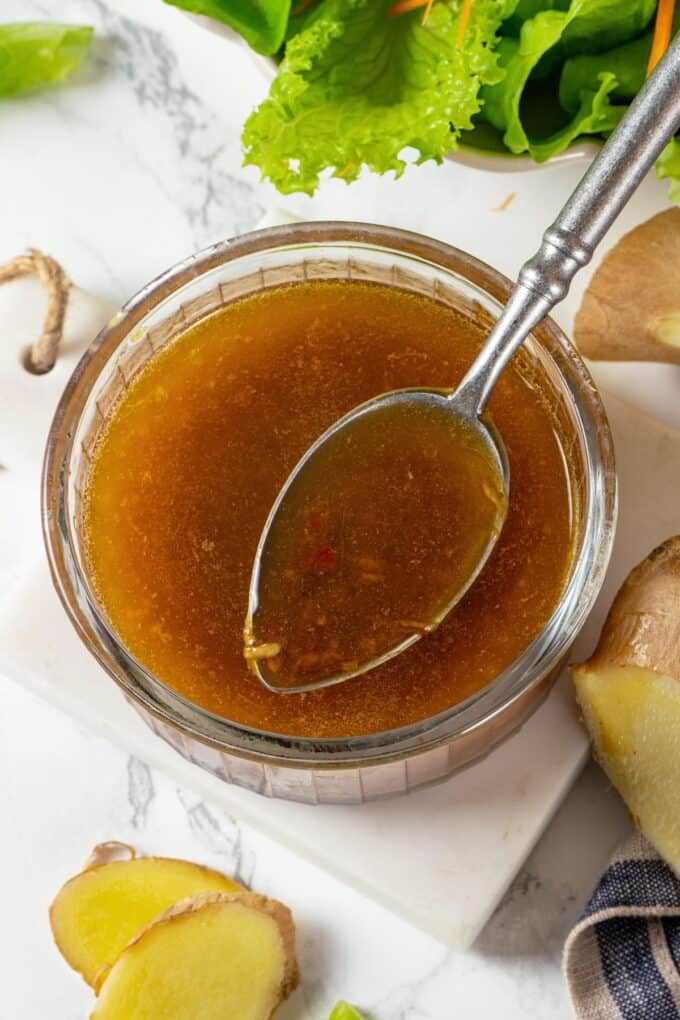 Close up of a spoon resting in a small glass bowl of a homemade soy ginger dressing.