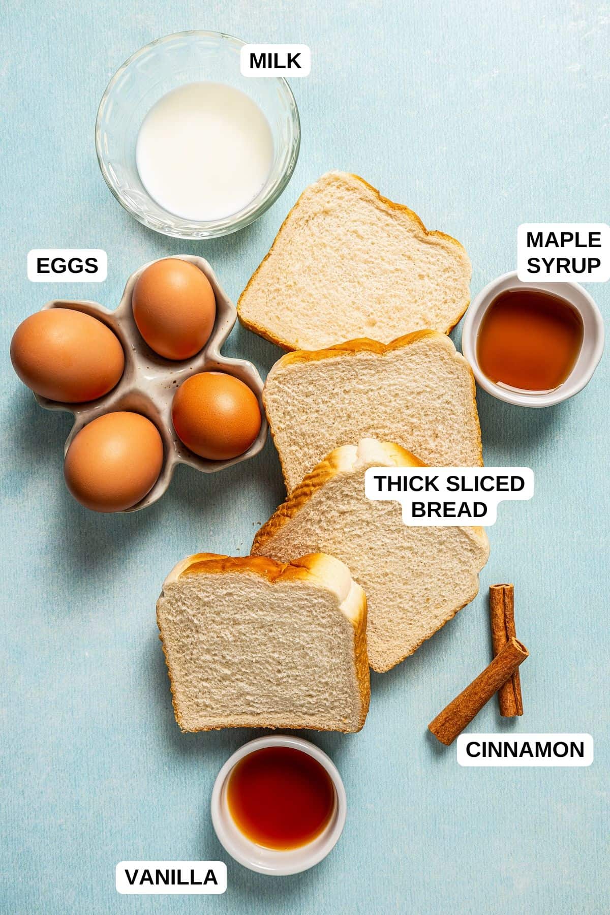Ingredients laid out on a counter for making French toast, including sliced bread, eggs, milk, maple syrup and vanilla.