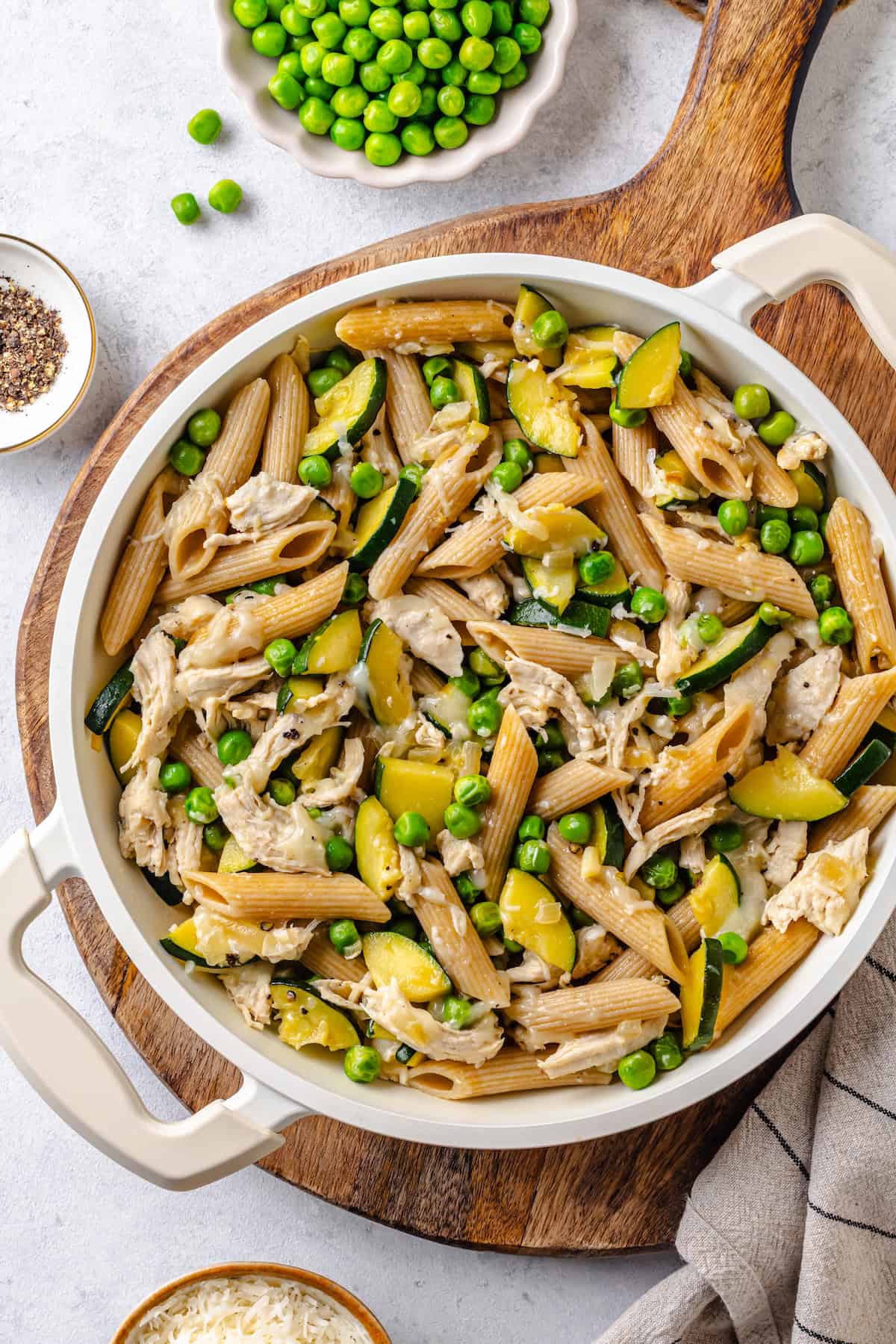 A cheesy healthy chicken pasta with zucchini and peas in a large white skillet.