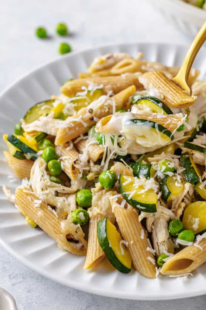 A forkful of a pasta chicken and zucchini mix being picked up from a plate.