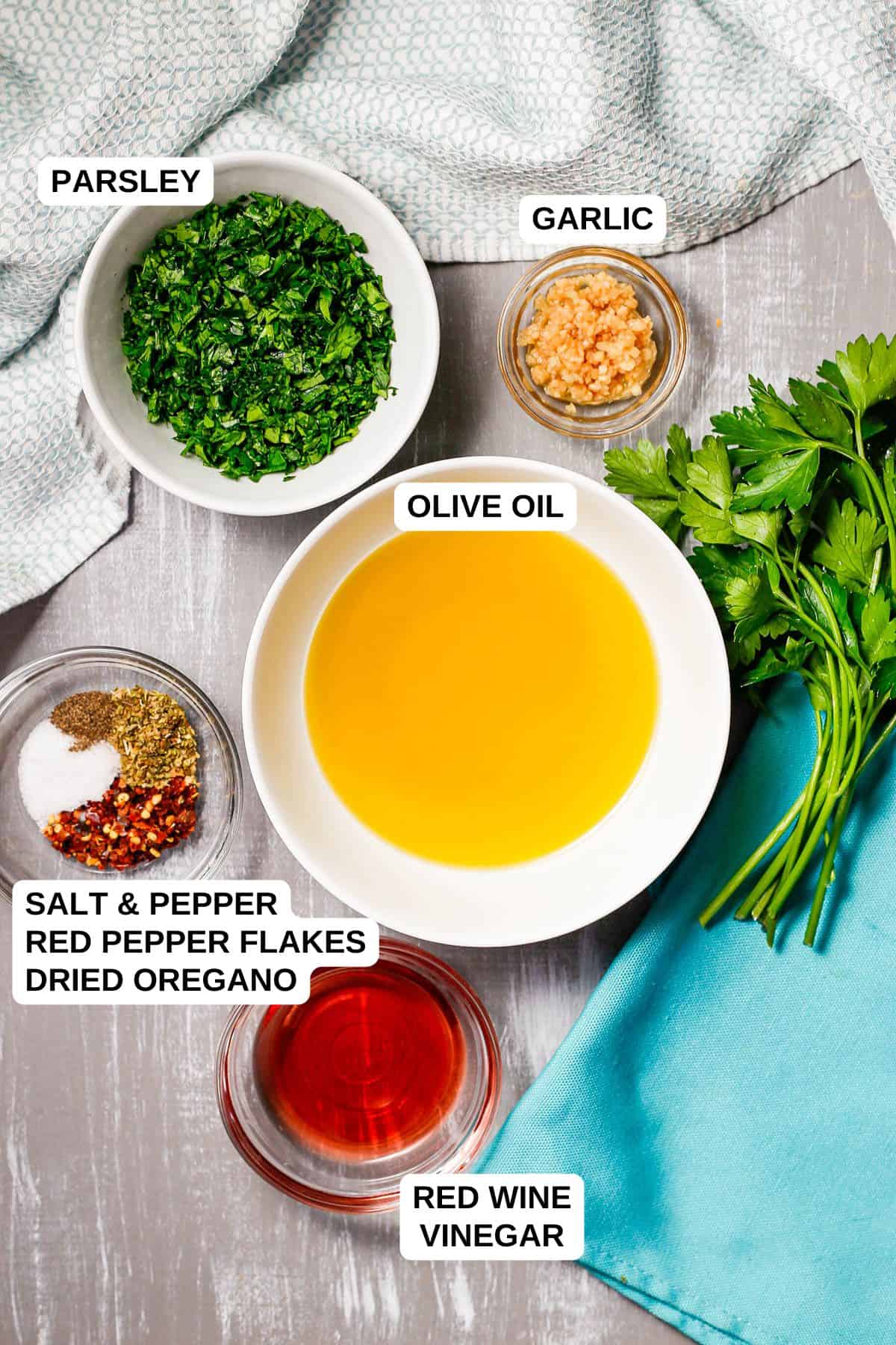 Ingredients laid out in separate bowls for making a green sauce, including parsley, garlic, olive oil, red wine vinegar and seasonings.