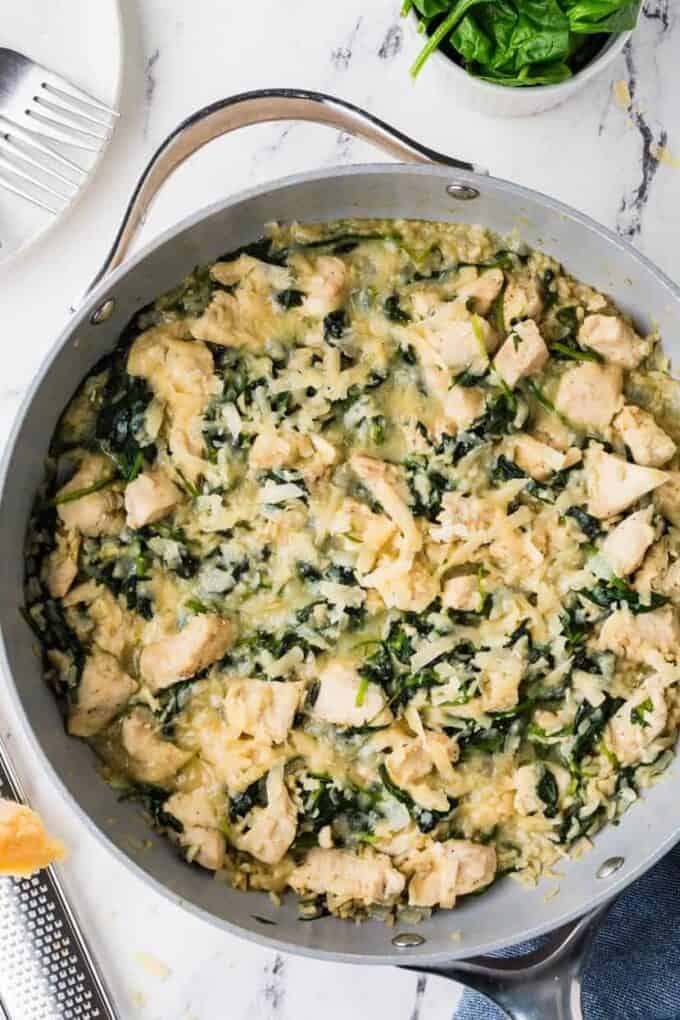 A cheesy chicken and brown rice skillet with spinach wilted in and fresh spinach to the side.