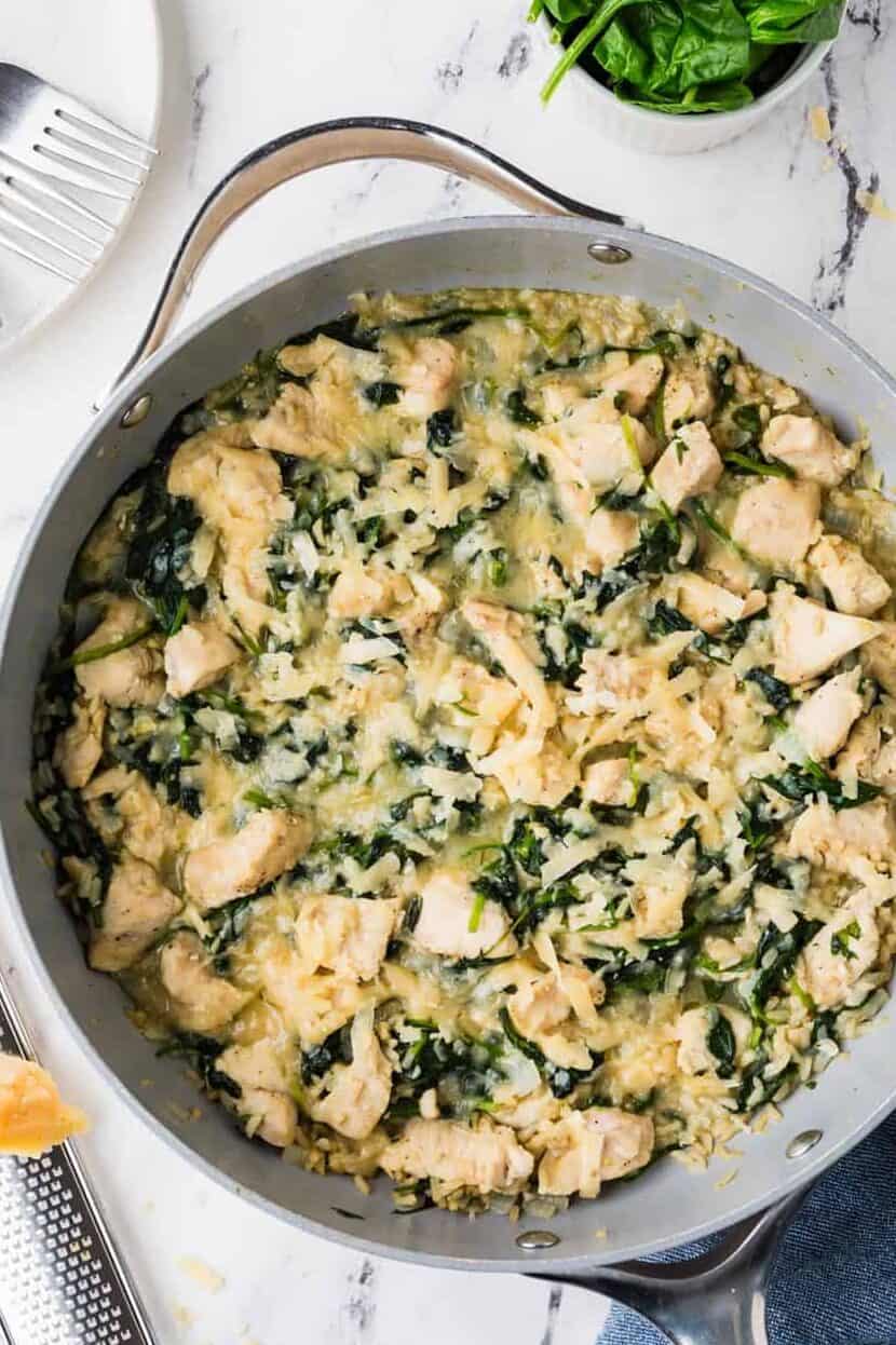 A cheesy chicken and brown rice skillet with spinach wilted in and fresh spinach to the side.