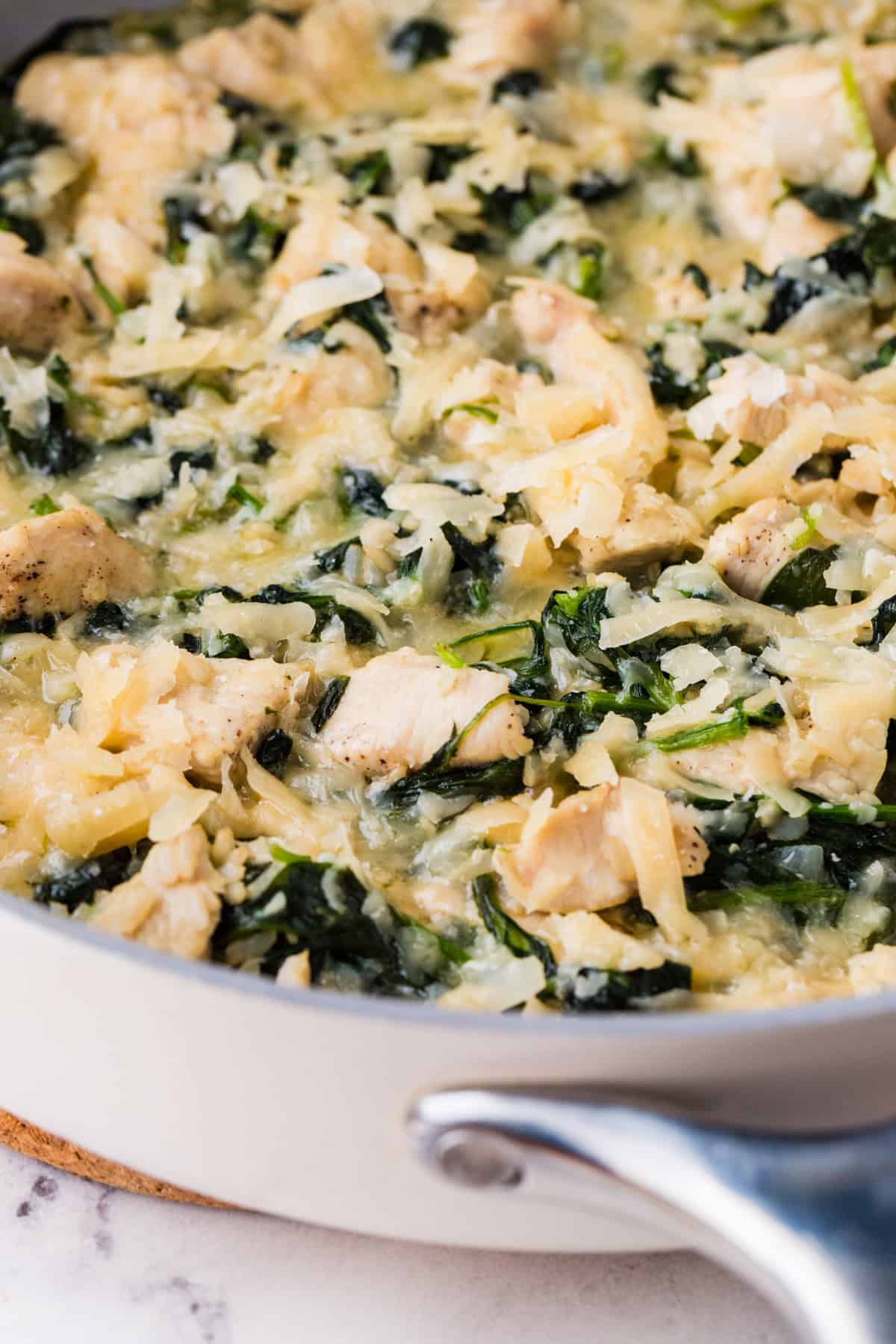 A side angle view of a skillet with a chicken Florentine dish with brown rice, spinach and Parmesan cheese.