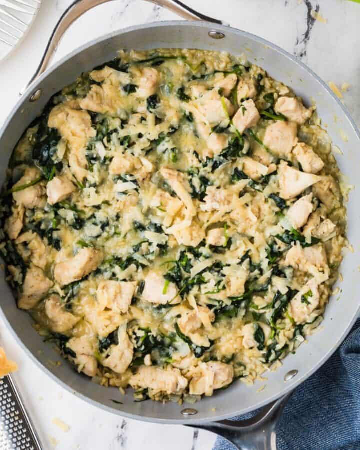 Close up of a cheesy chicken and brown rice skillet with spinach wilted in.