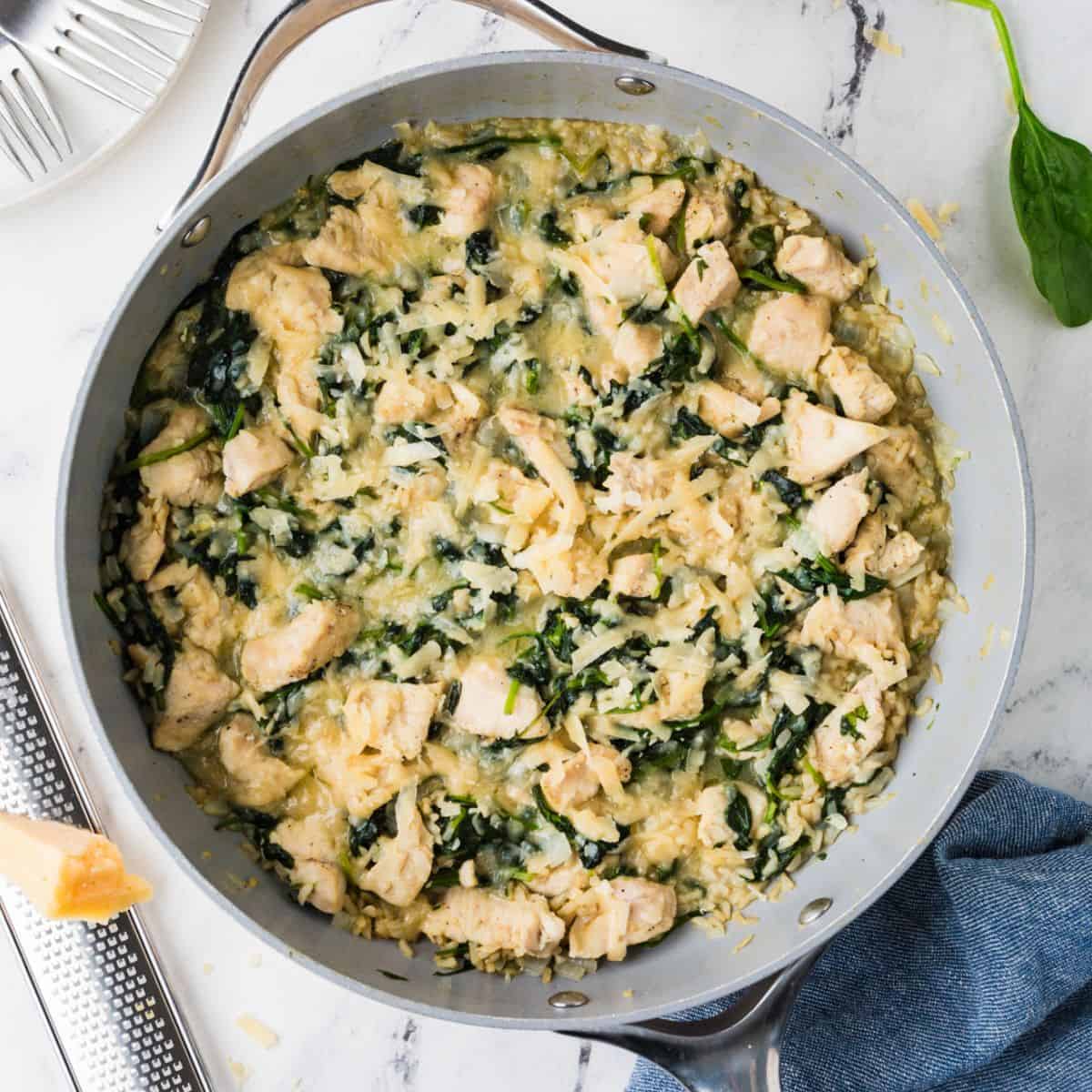 Close up of a cheesy chicken and brown rice skillet with spinach wilted in.