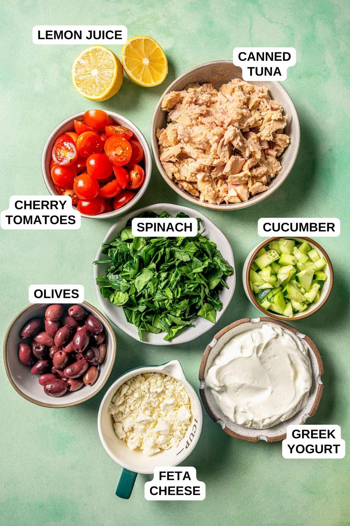 Ingredients laid out in separate bowls for making a tuna salad with tomatoes, spinach, cucumbers, olives and feta cheese.