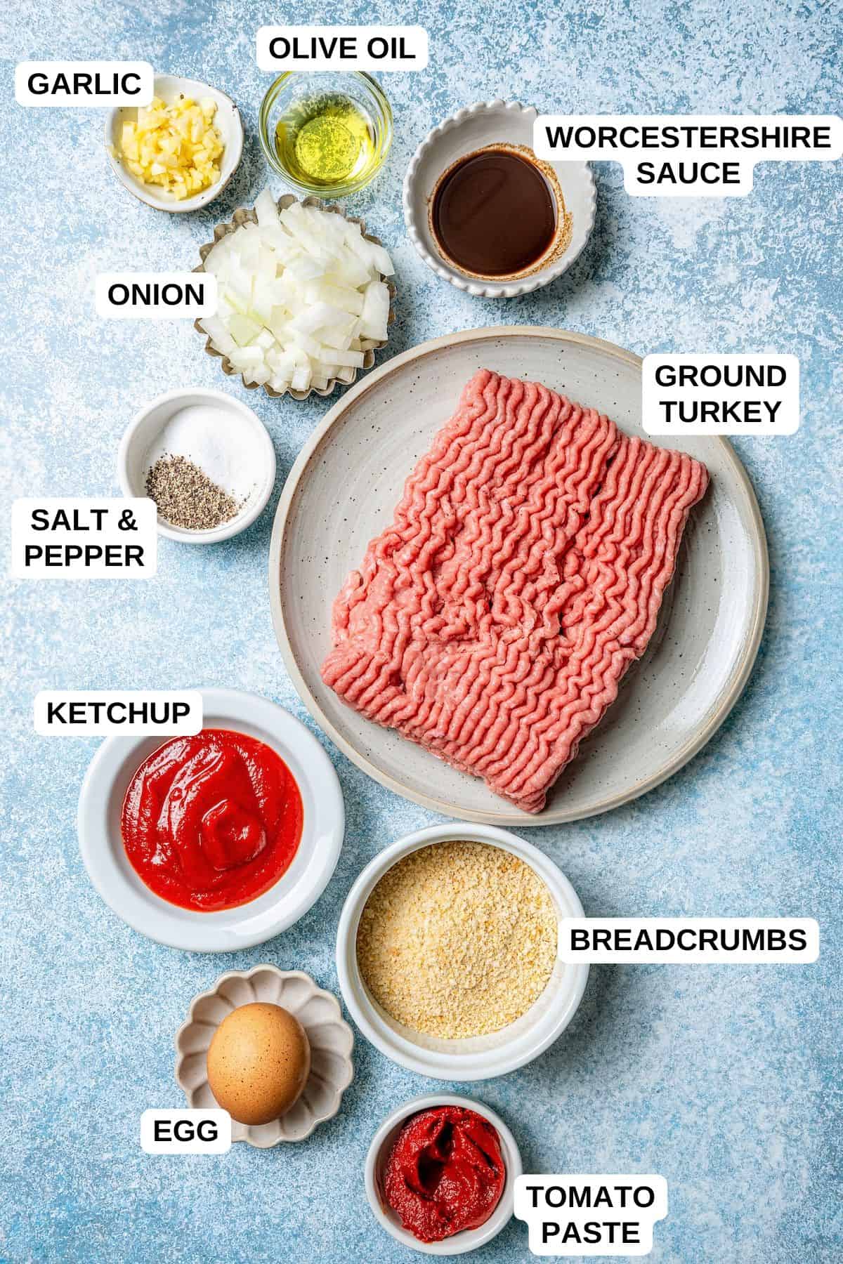 Ingredients laid out in separate containers for making a meatloaf recipe, including ground turkey, ketchup, breadcrumbs, onion and seasonings.