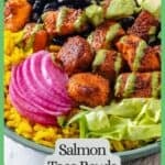 Close up of a green bowl with yellow rice topped with piles of black beans, salmon bites, chopped lettuce, pickled red onion, diced avocado and cilantro dressing drizzled on top with a border and text around the photo.