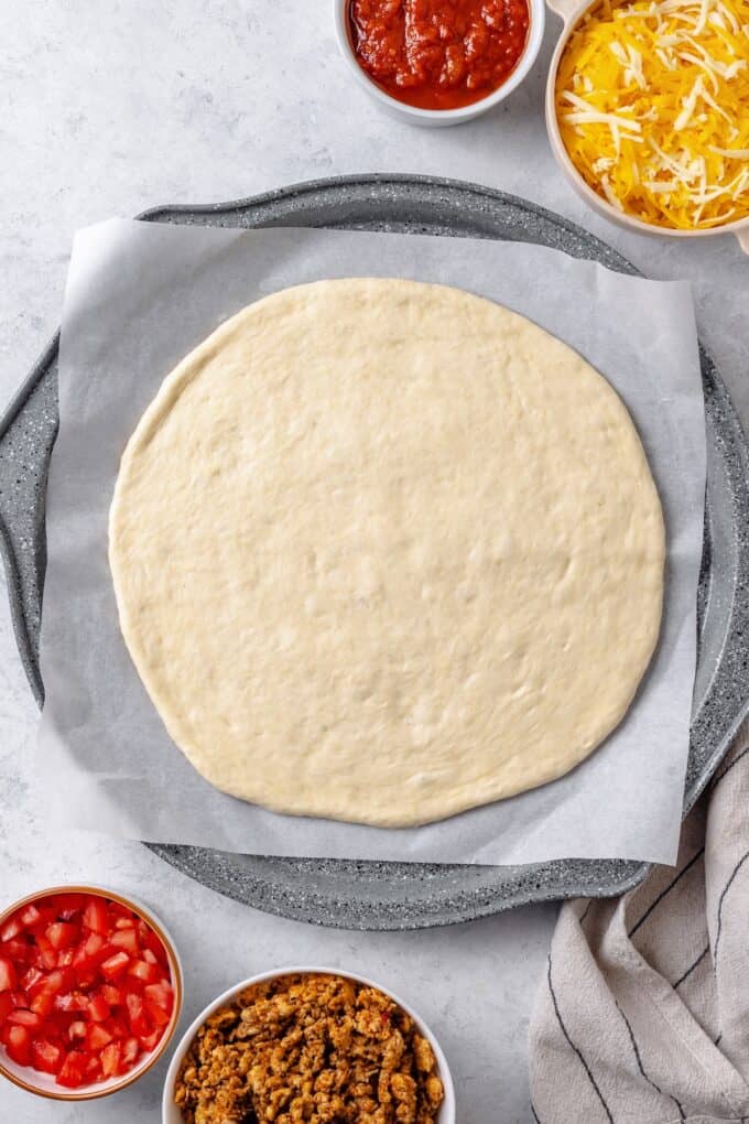 Pizza dough rolled out on a parchment paper lined pizza pan.