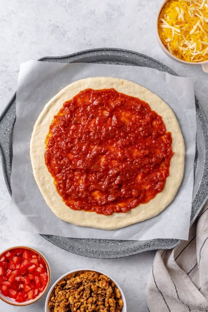 Pizza sauce spread out on a rolled out pizza dough on a pizza pan.