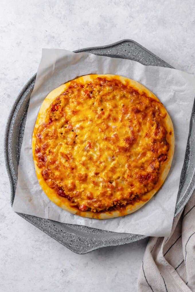 A baked cheesy taco pizza on a parchment paper lined pizza pan.