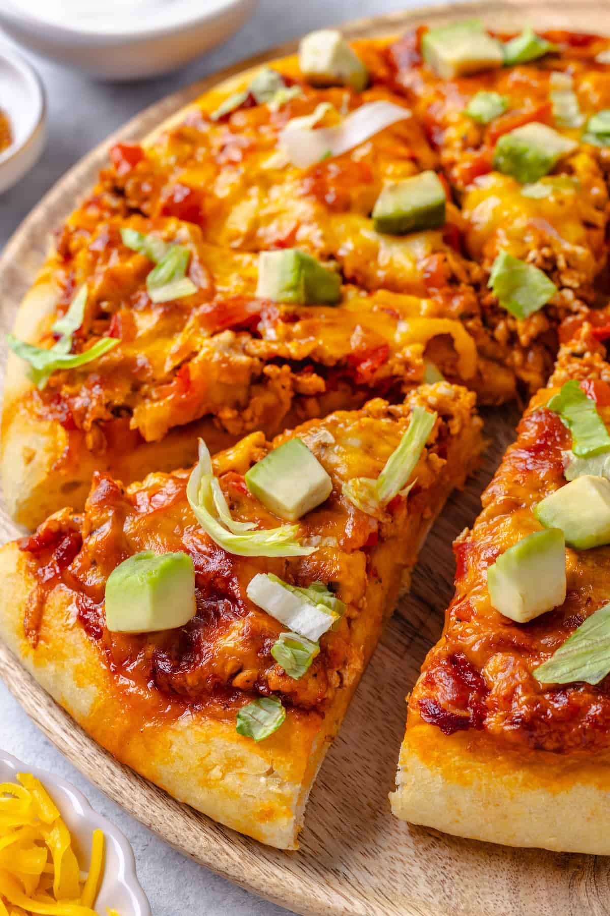 A slice of taco pizza pulled away from the cut pizza.