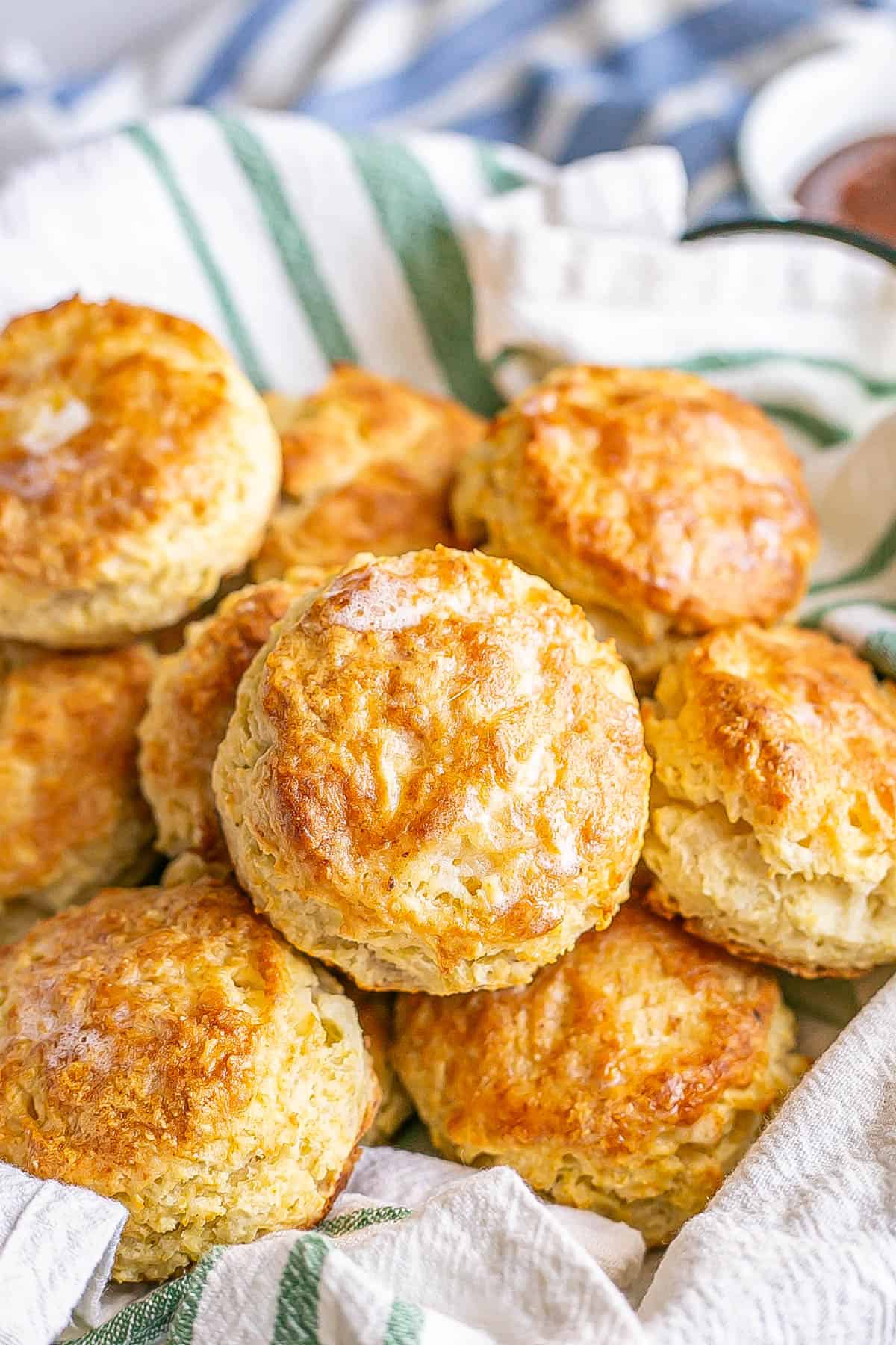 A green striped towel lining a basket full of buttery homemade biscuits stacked in.