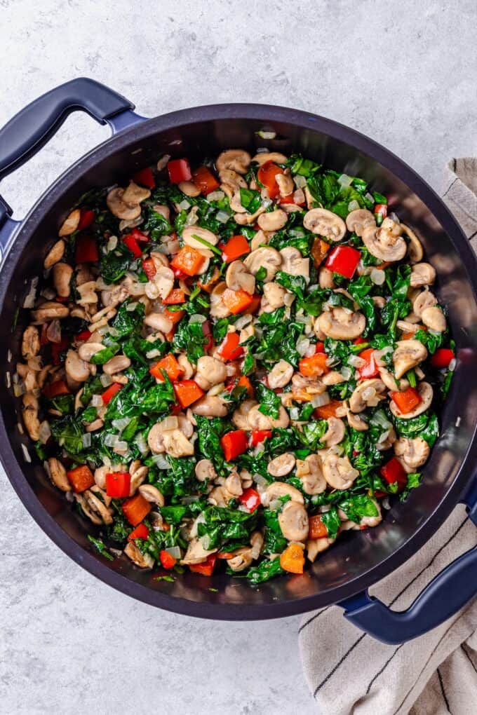 A large skillet with a mix of sautéed mushrooms, red pepper and spinach.