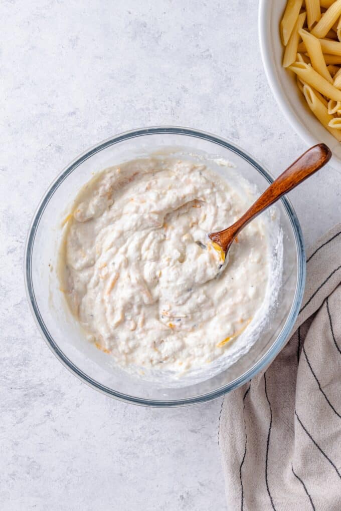 A clear bowl with a cottage cheese mixture with a wooden spoon resting in it.