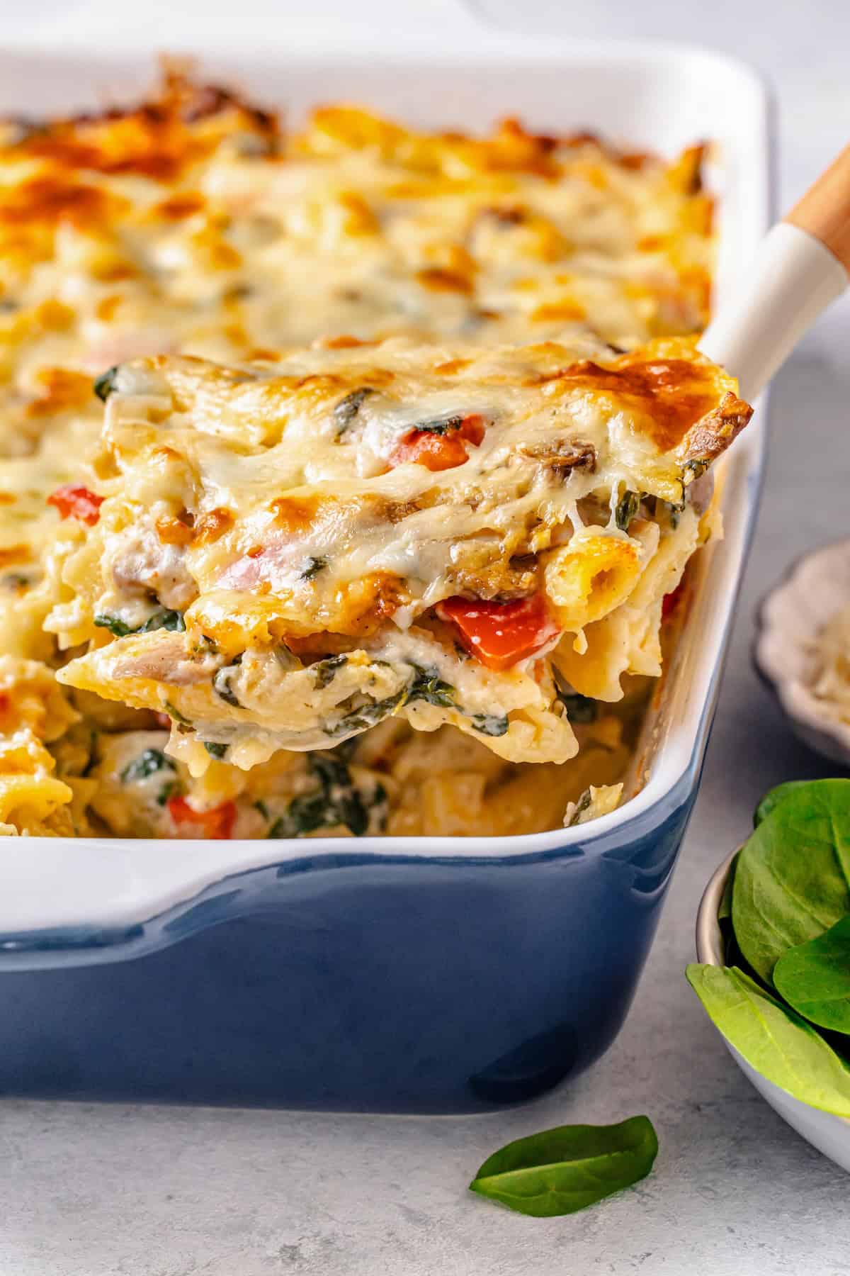 A scoop of a chicken and pasta baked casserole being lifted out of a blue and white casserole dish.