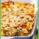 A scoop of a chicken and pasta baked casserole being lifted out of a blue and white casserole dish with a green border and a text overlay around the photo.