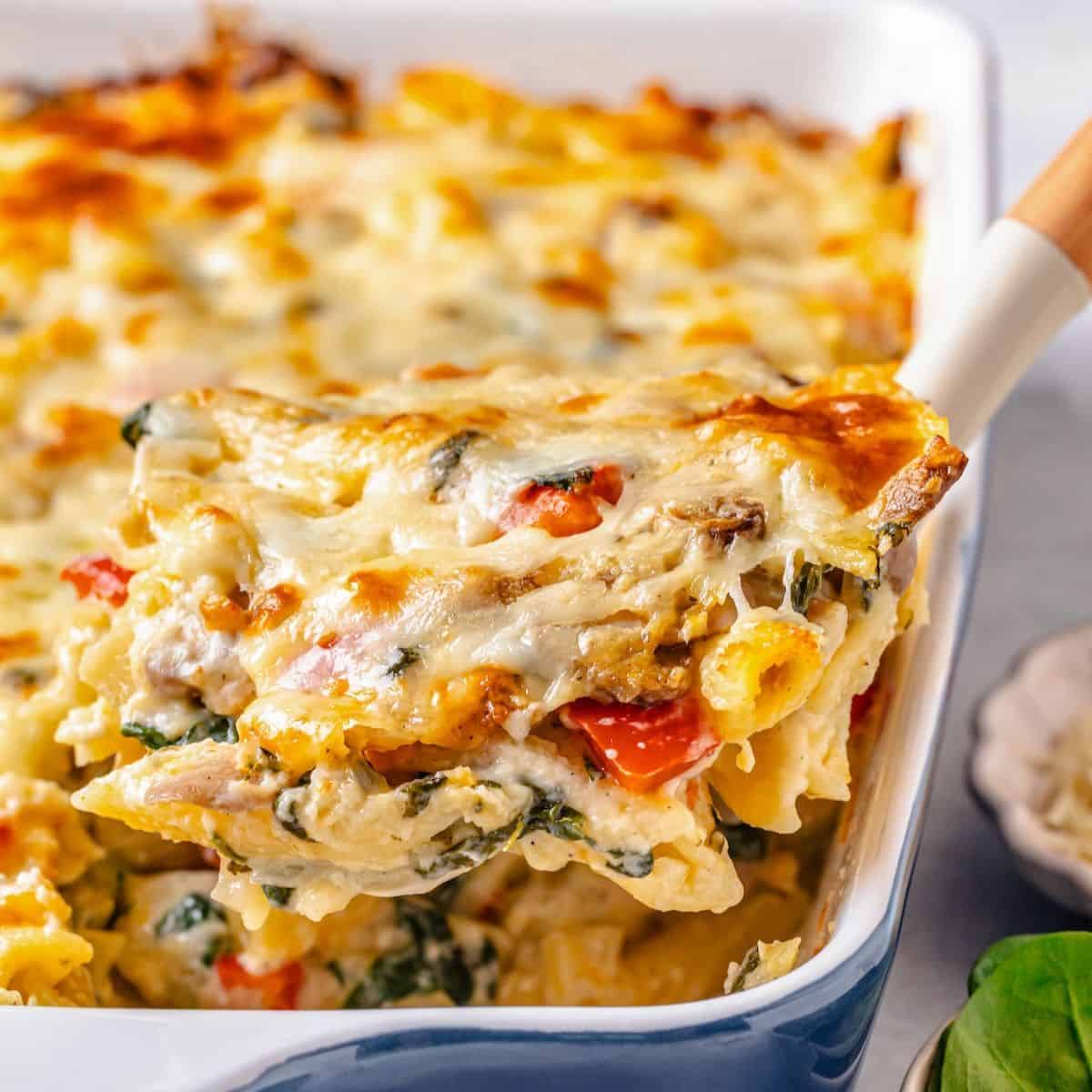Close up of a scoop of a chicken and pasta baked casserole being lifted out of a blue and white casserole dish.