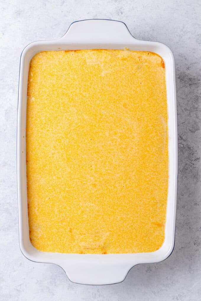 Cornbread batter spread over a layer of chili in a white casserole dish.