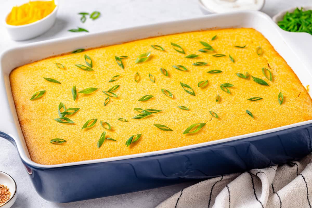 A rectangular blue casserole dish with a cornbread topped chili bake in it and sliced green onions sprinkled on top.