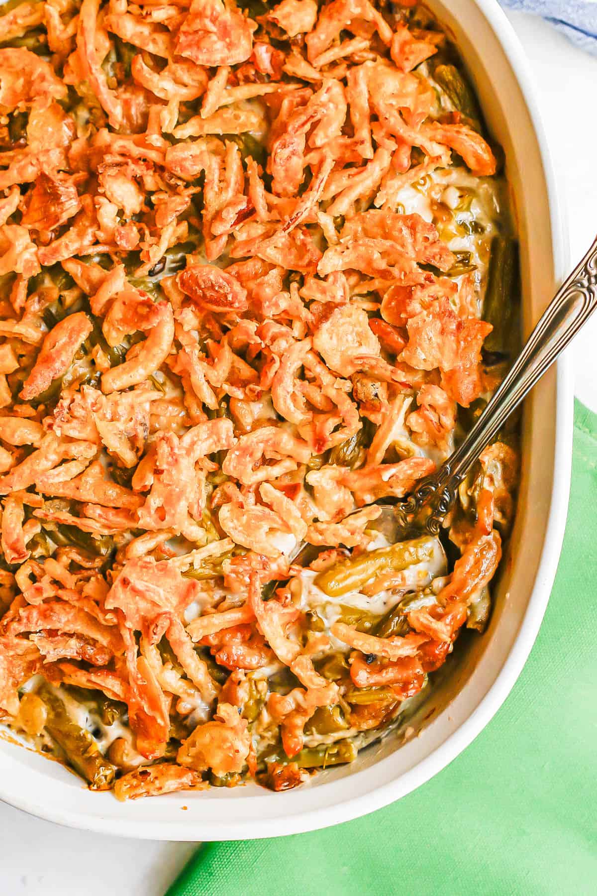 Close up of a silver spoon resting in a white baking dish full of a green bean casserole with French fried onions on top.