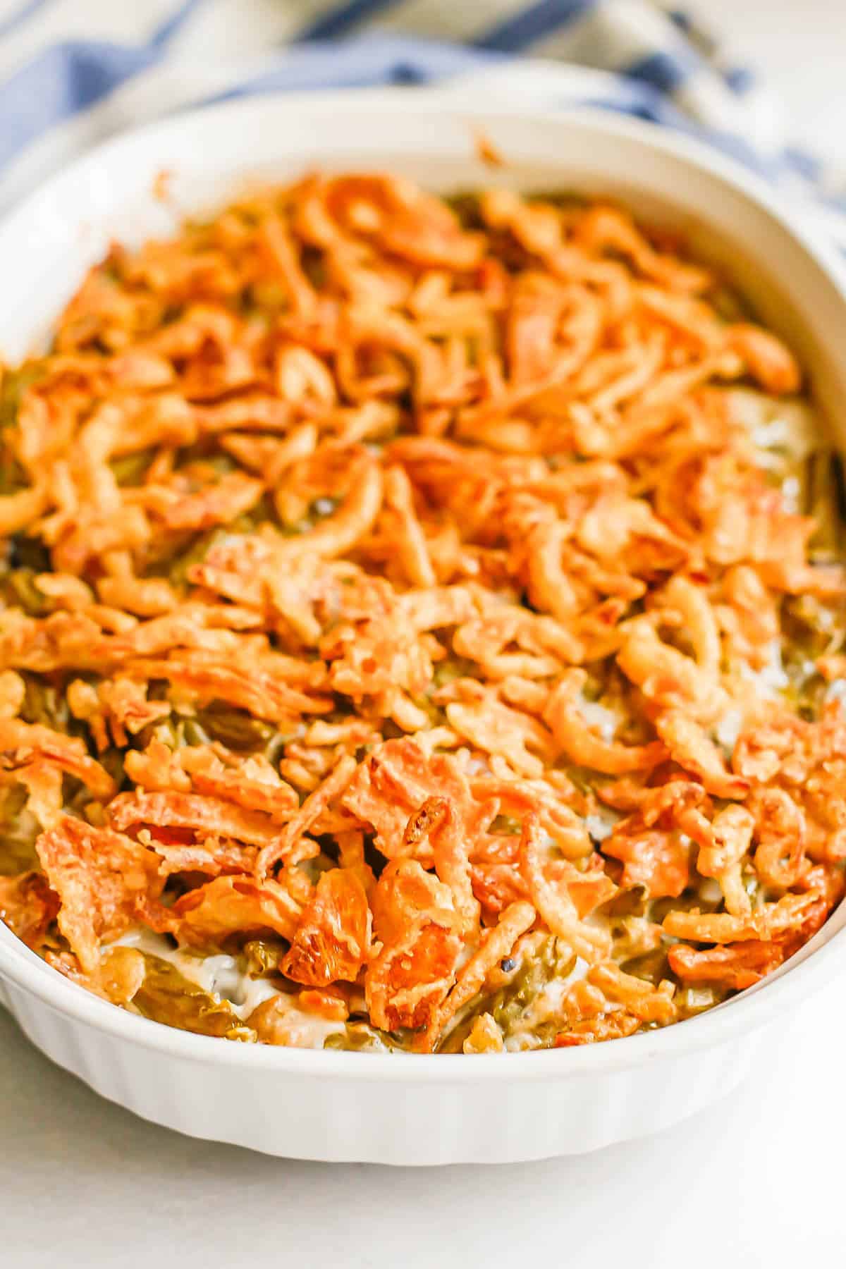 Fried onions on top of a creamy green bean mixture in a white oval baking dish.
