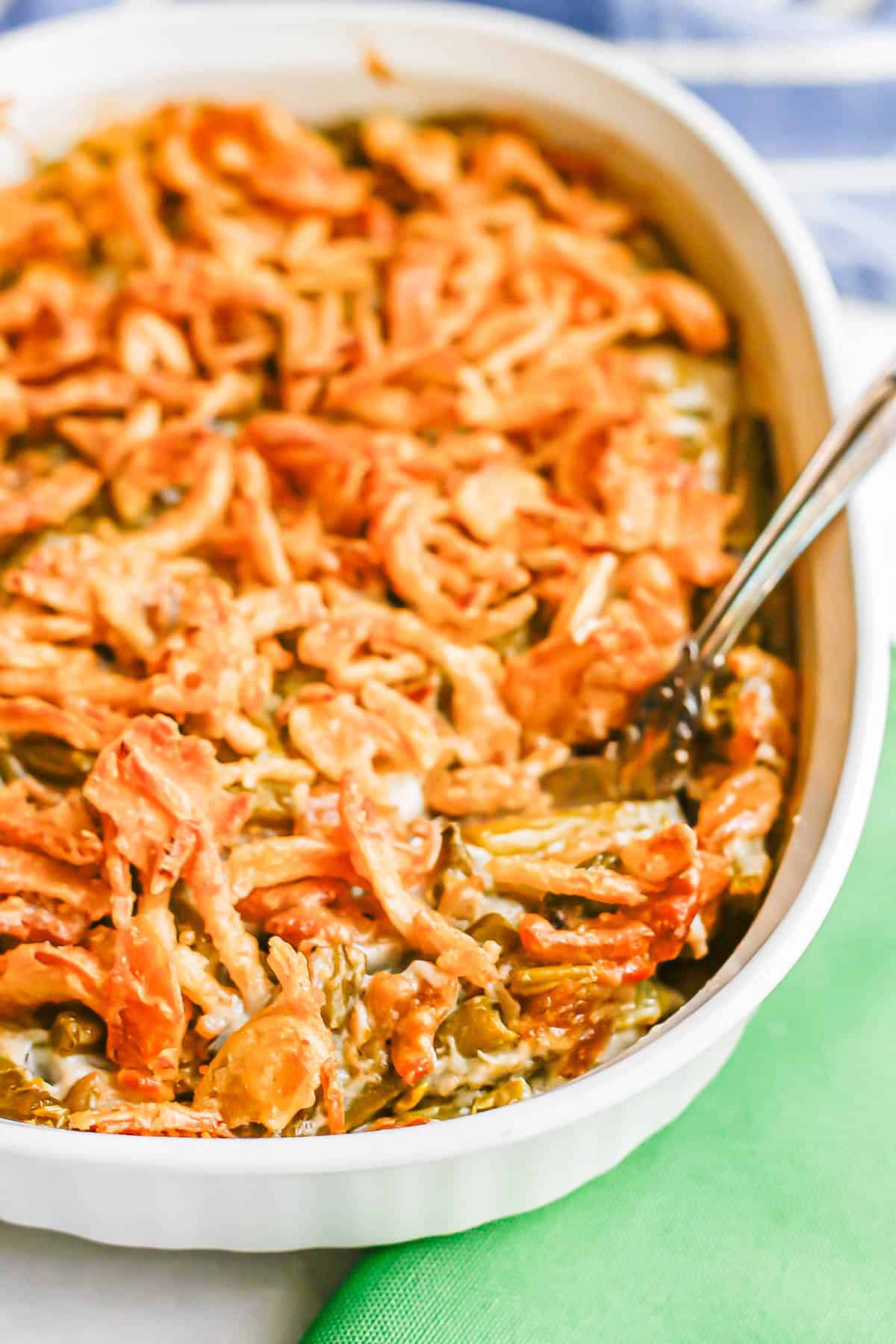 A serving spoon resting in a white baking dish full of a green bean casserole with French fried onions on top.