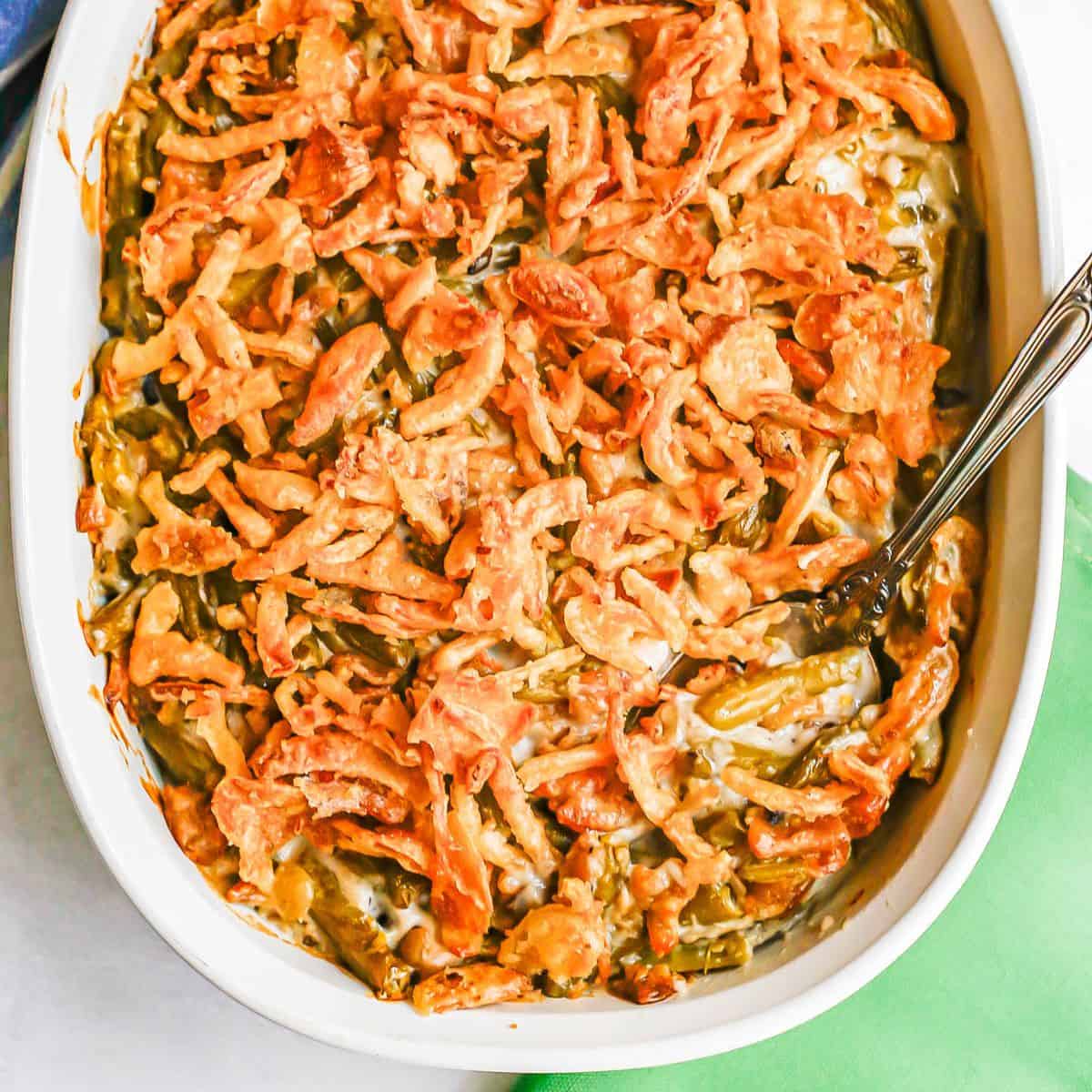 Close up of a serving spoon resting in a white baking dish full of a green bean casserole with French fried onions on top.