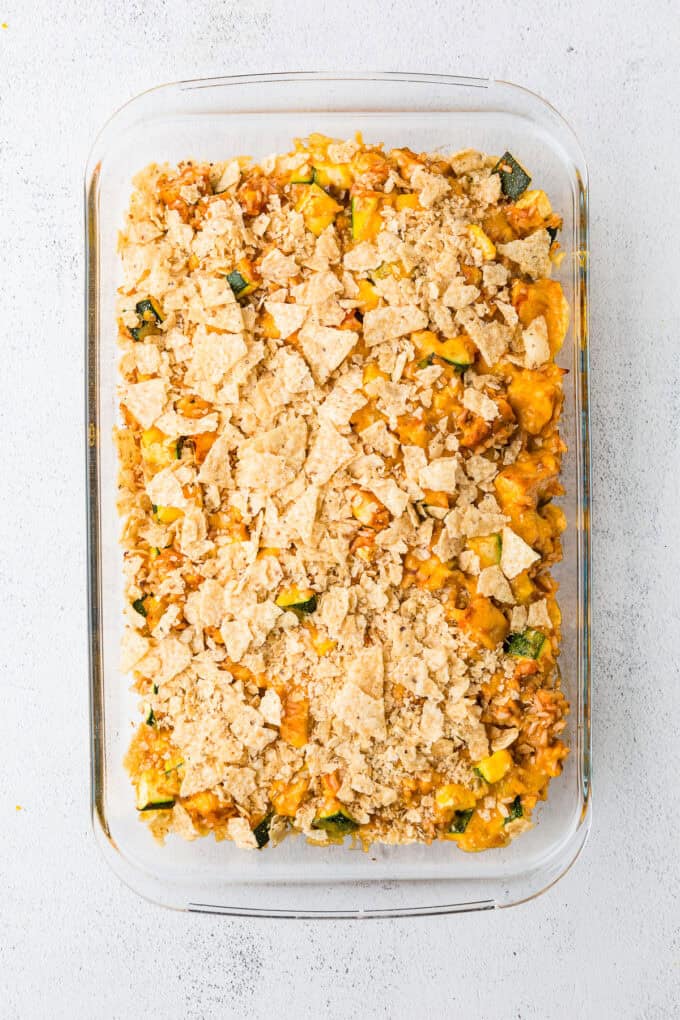 A glass casserole dish with a chicken, rice and veggie mix spread out with shredded cheddar cheese and tortilla chips on top.