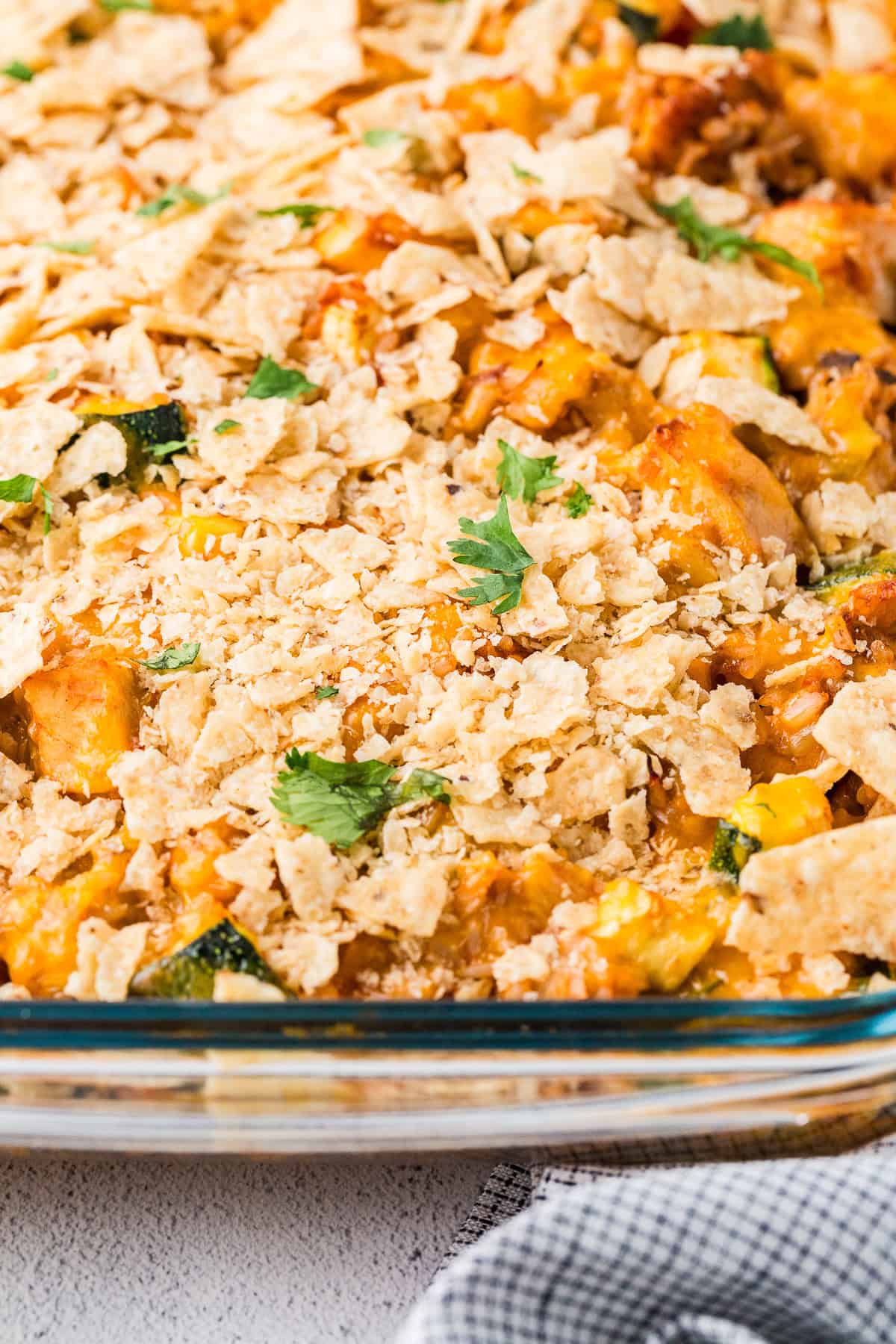 Close up of a baked chicken taco casserole with cheese and tortilla chips on top in a glass baking dish with sprinkled cilantro on it.