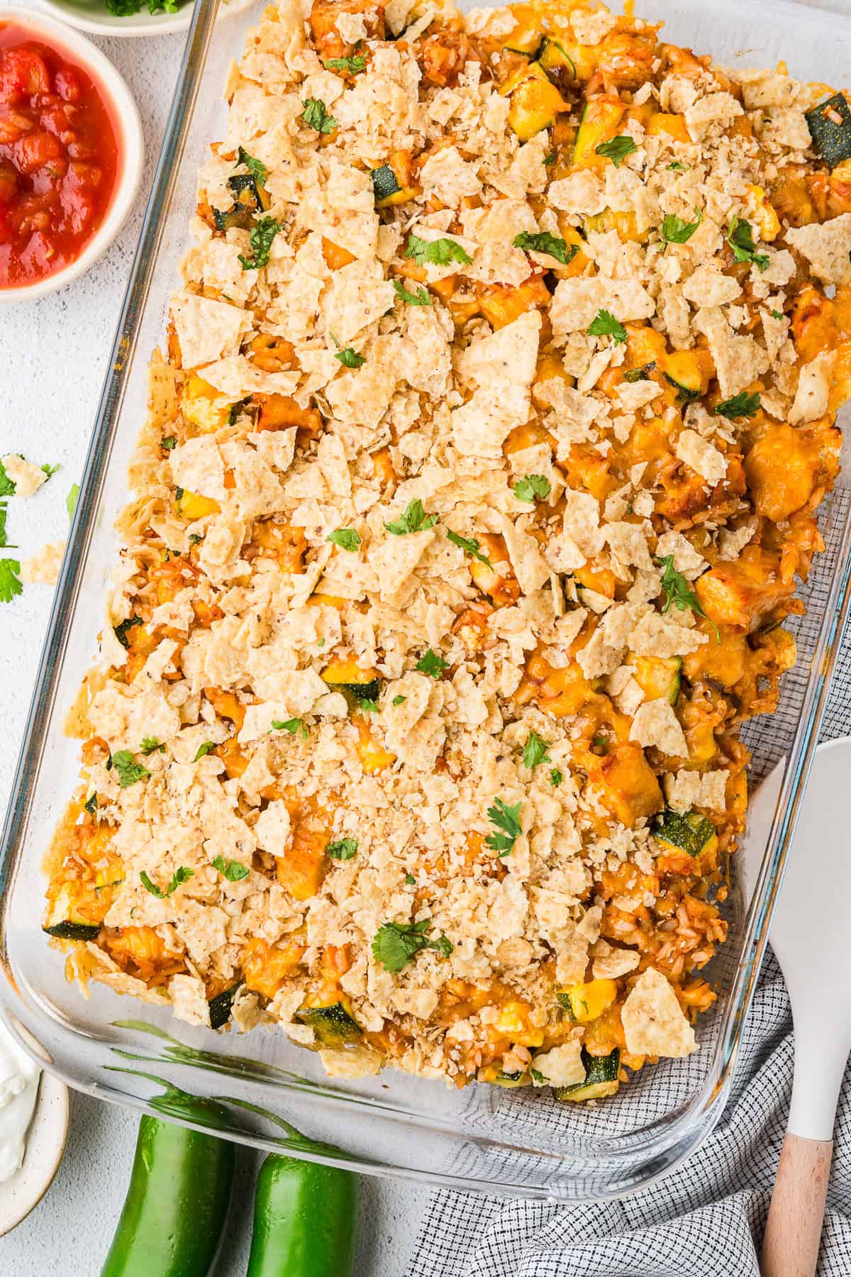 A baked chicken taco casserole with cheese and tortilla chips on top in a glass baking dish with sprinkled cilantro on top.