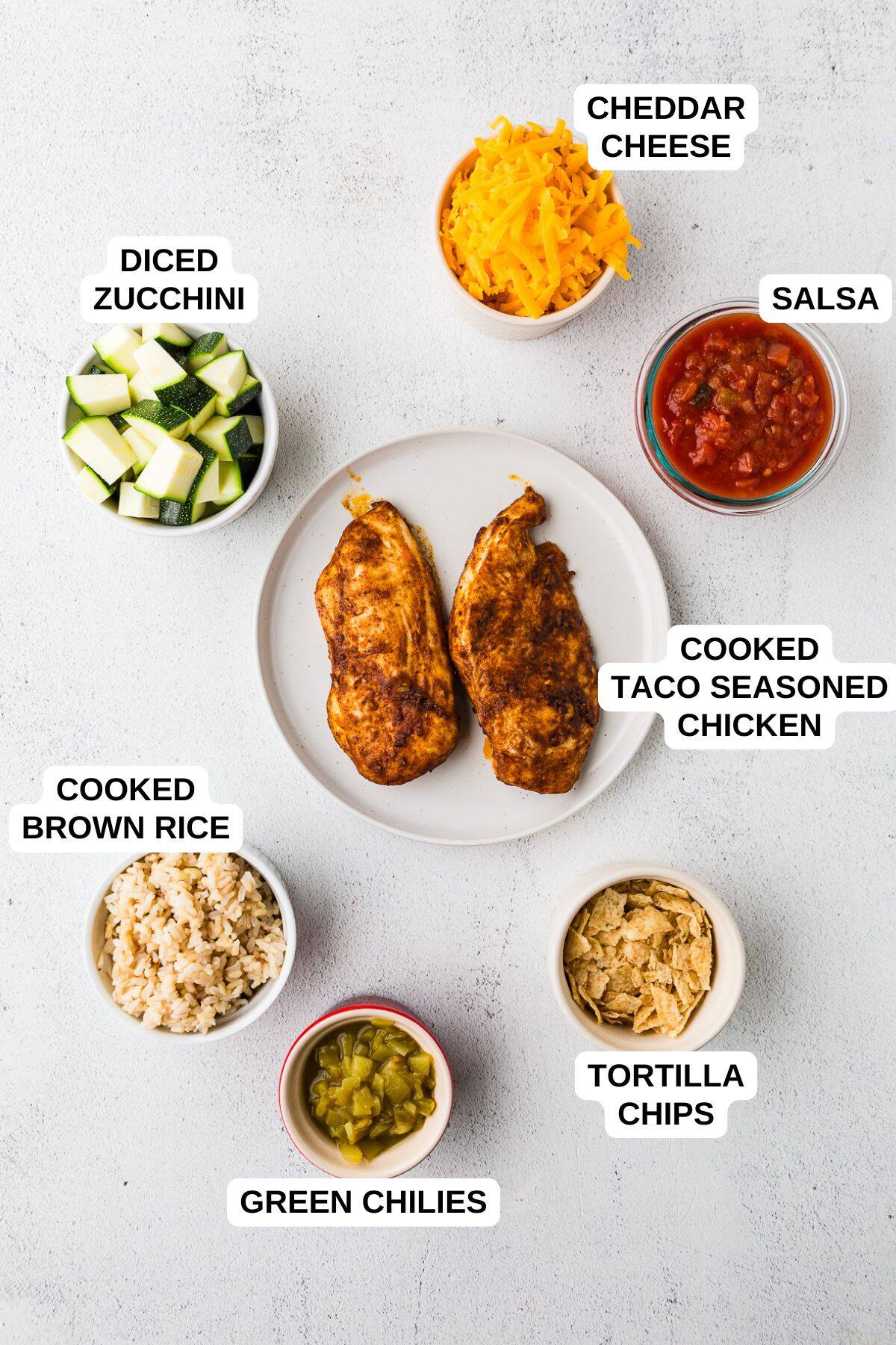 Ingredients laid out in separate bowls for making a taco chicken casserole with brown rice, zucchini and cheese.