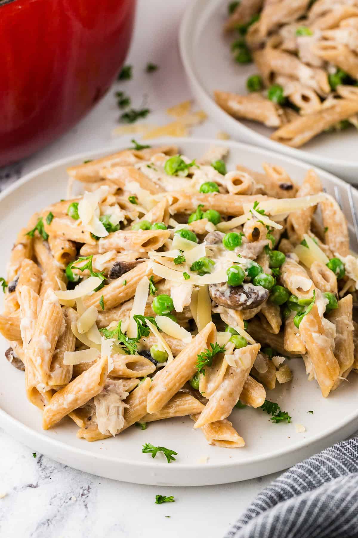 Pasta with chicken, mushrooms and peas served on a round white plate with cheese sprinkled on top.