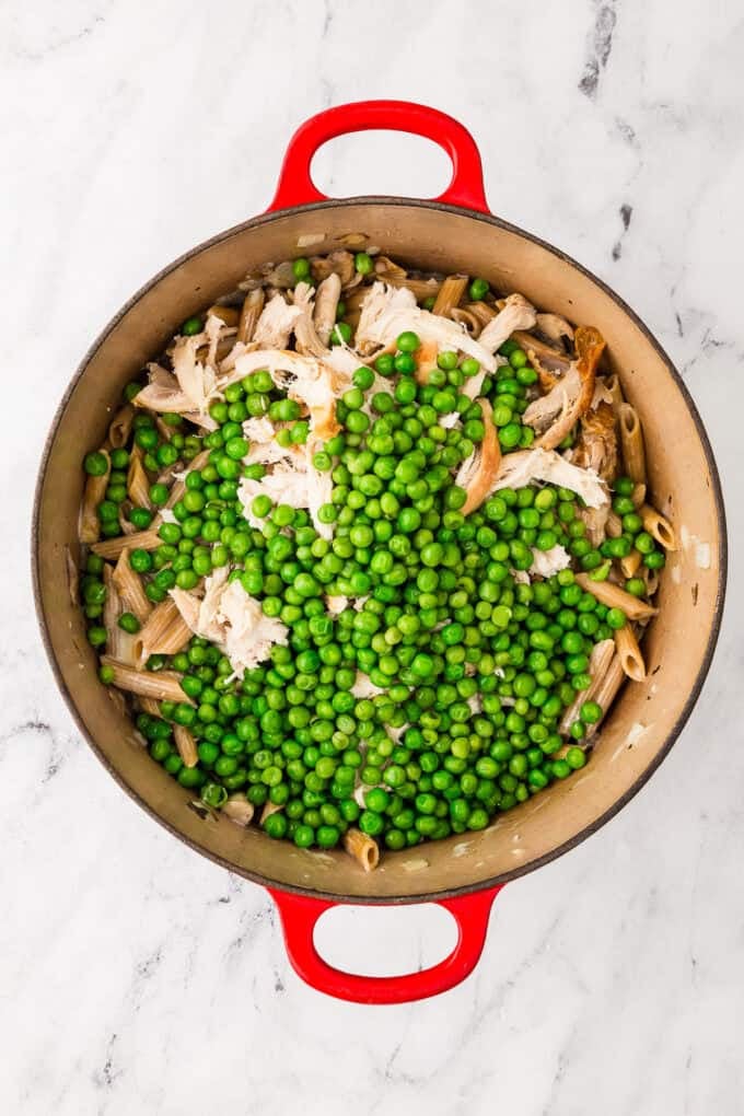 Green peas added on top of a chicken pasta mixture in a large red pan.