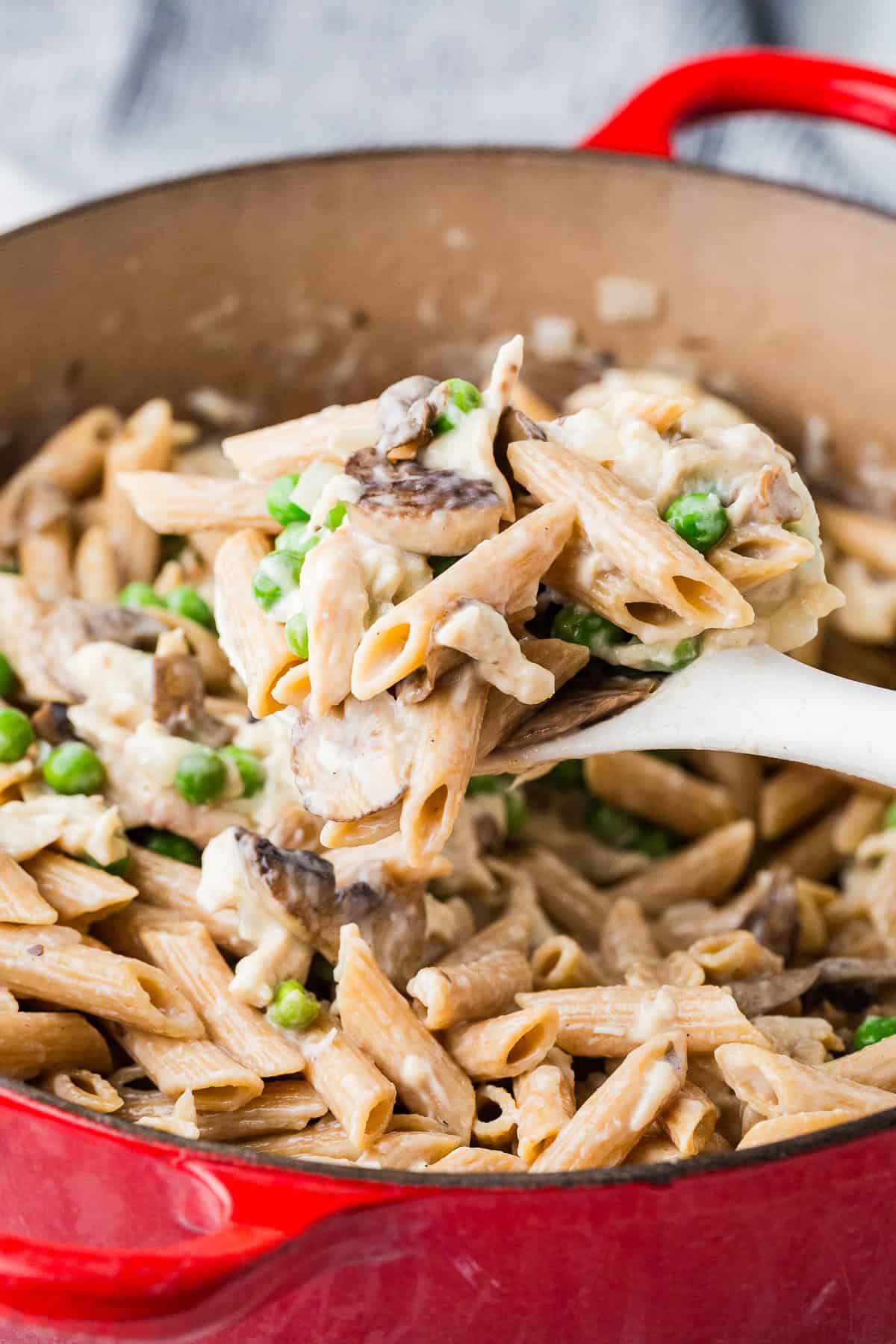 A spoon lifting up a serving of a creamy one pot pasta with chicken, mushrooms and peas.