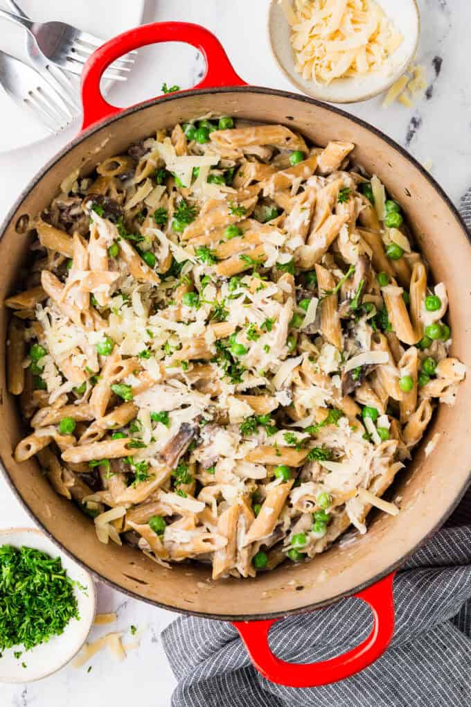 A large red pot with a one pasta pasta with chicken, mushrooms, peas and cheese.