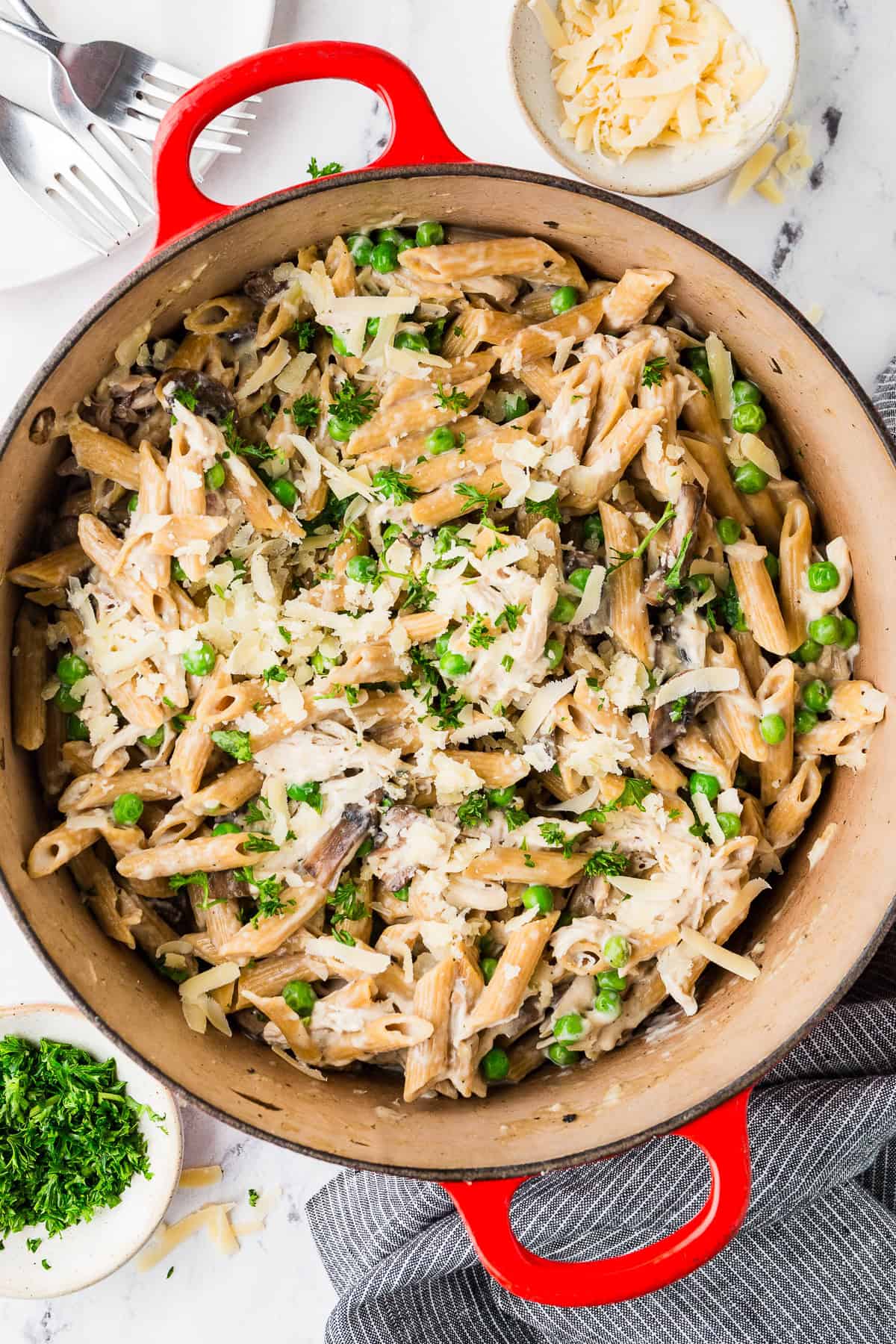 A large red pot with a one pasta pasta with chicken, mushrooms, peas and cheese.
