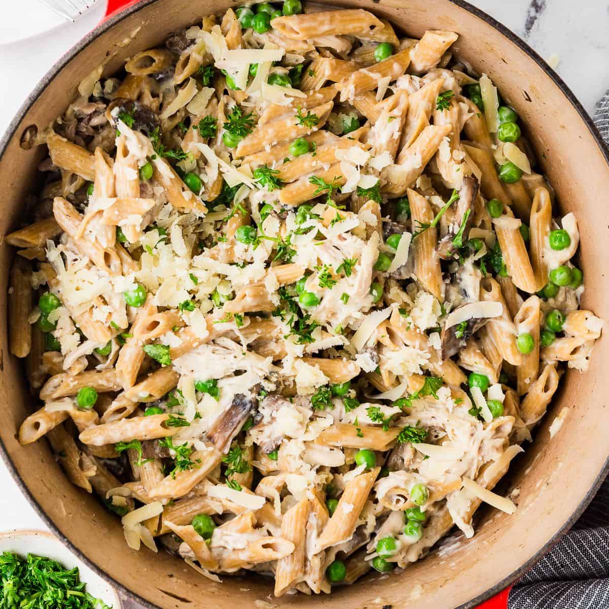 Close up of a large red pot with a one pasta pasta with chicken, mushrooms, peas and cheese.