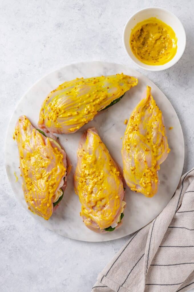 Stuffed chicken breasts brushed with a mustard mixture on a plate.
