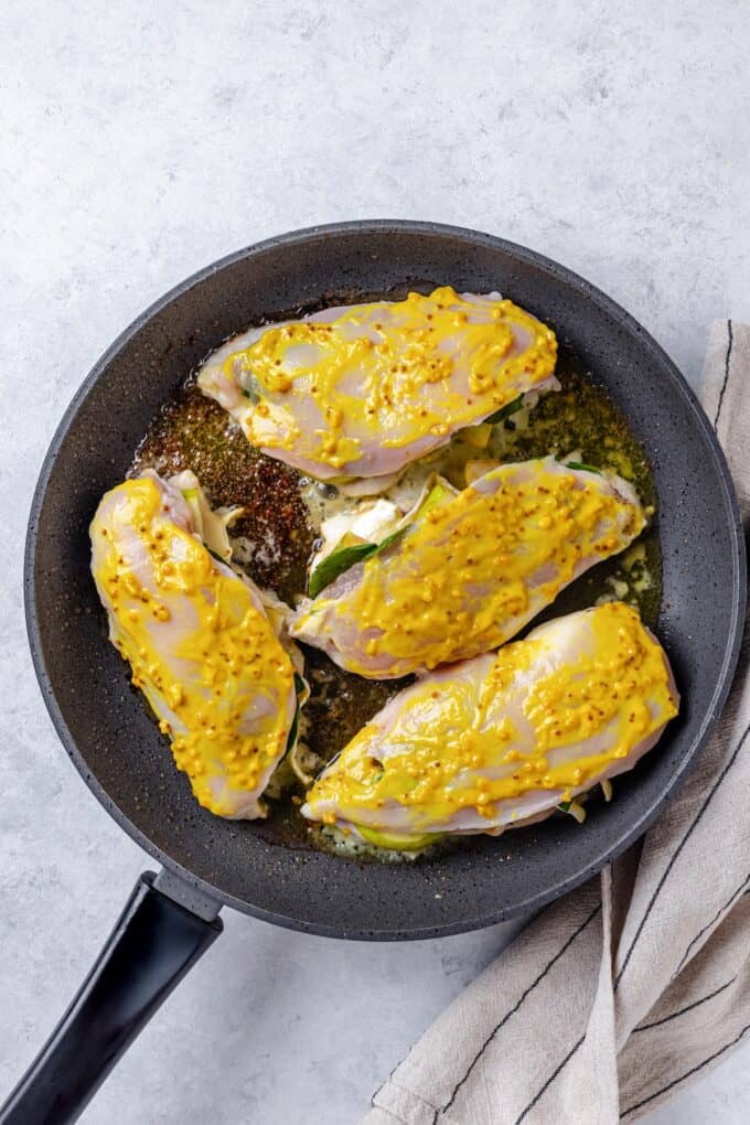 Stuffed chicken breasts brushed with a mustard mixture being cooked in a skillet.