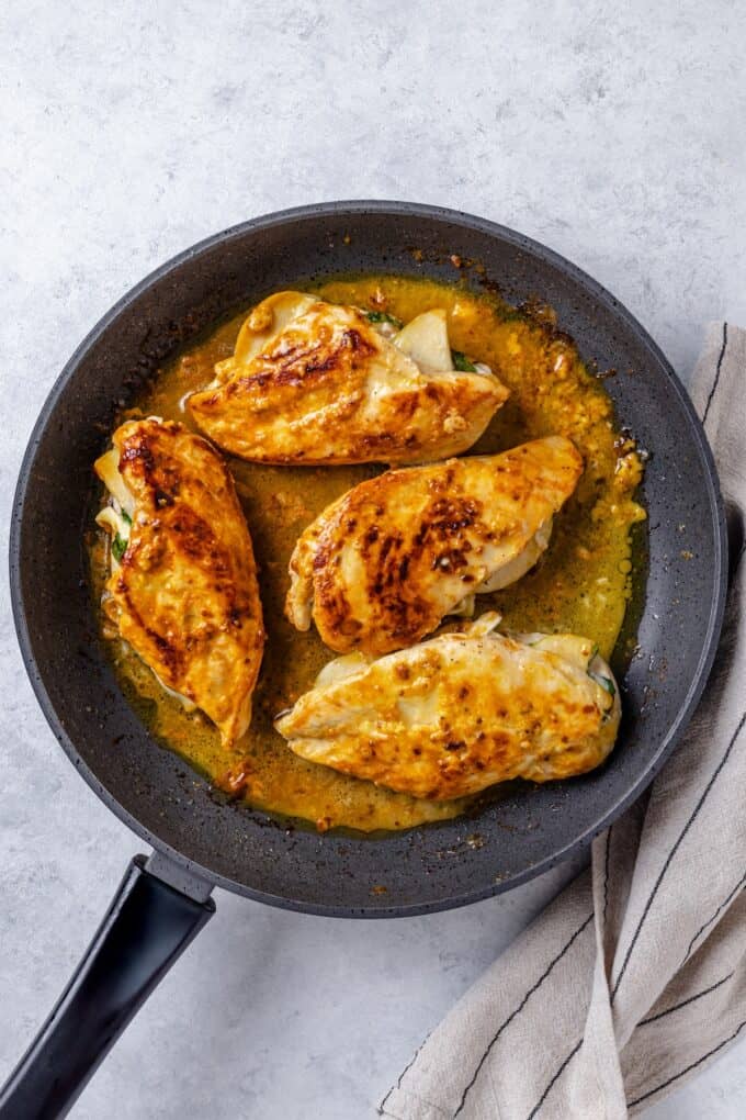Cooked chicken breasts in a skillet stuffed with brie cheese and apples.