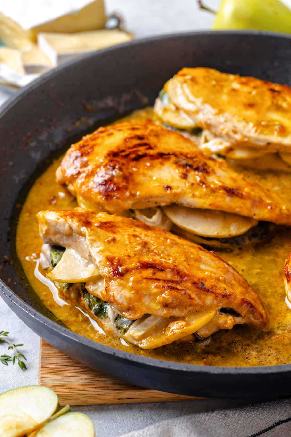 Close up of apple and brie stuffed chicken breasts in a pan sauce in a skillet.